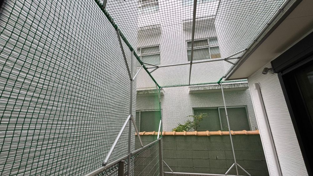 住宅ベランダの空間に合わせて専用の金属フレームを組み、緑色のネットで全体を覆った施工完了の様子です。
