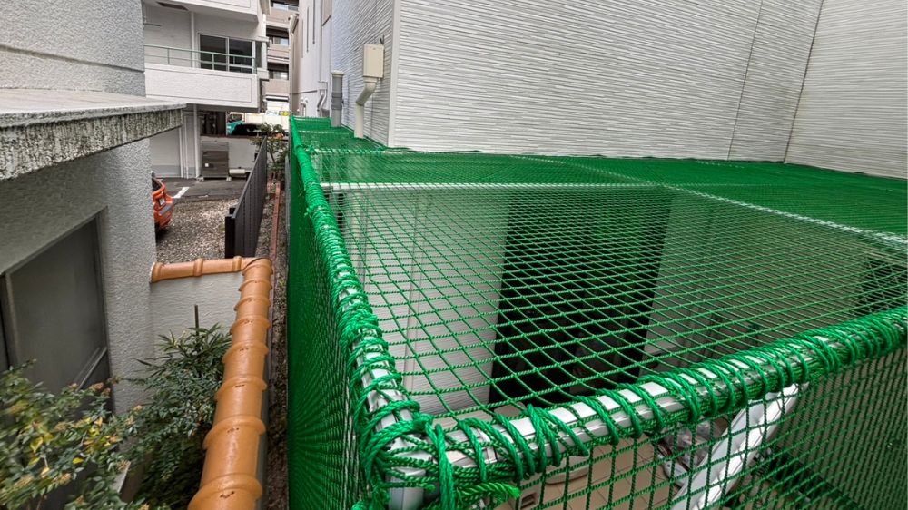 住宅脇の通路やベランダの上部を完全に塞ぐように、緑色の防鳥ネットを天井面にも水平に設置した様子