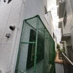 現代的な住宅の外壁に沿って設置された、猫の脱走を防ぐ緑色ネットの立体的な施工事例の全体像です。