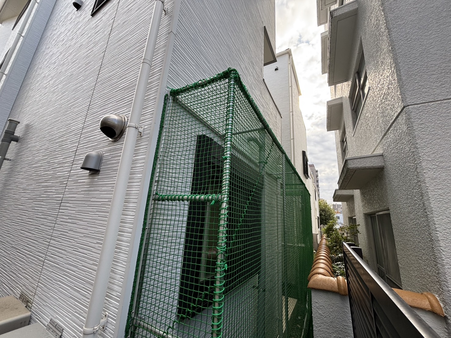 現代的な住宅の外壁に沿って設置された、猫の脱走を防ぐ緑色ネットの立体的な施工事例の全体像です。