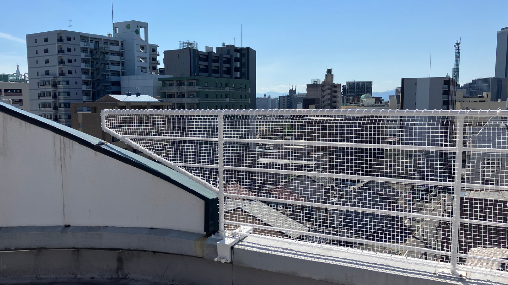 ビル屋上の手すり沿いに白い落下防止ネット。手摺の形状に合わせて斜めに設置された様子